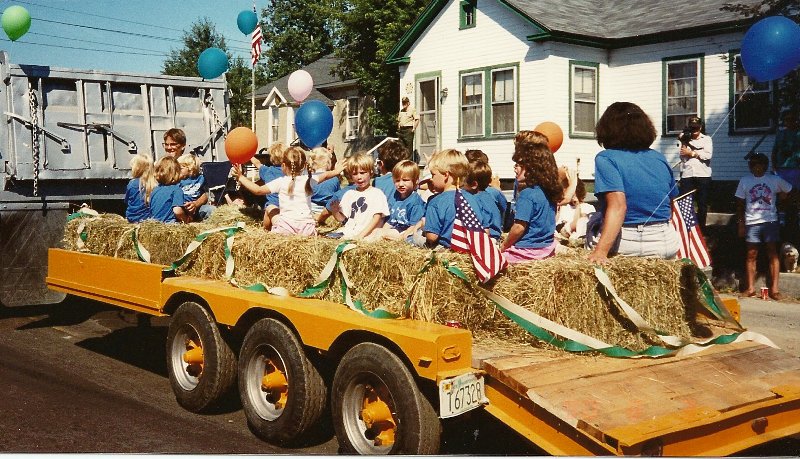 children riding on haybale covered parade float