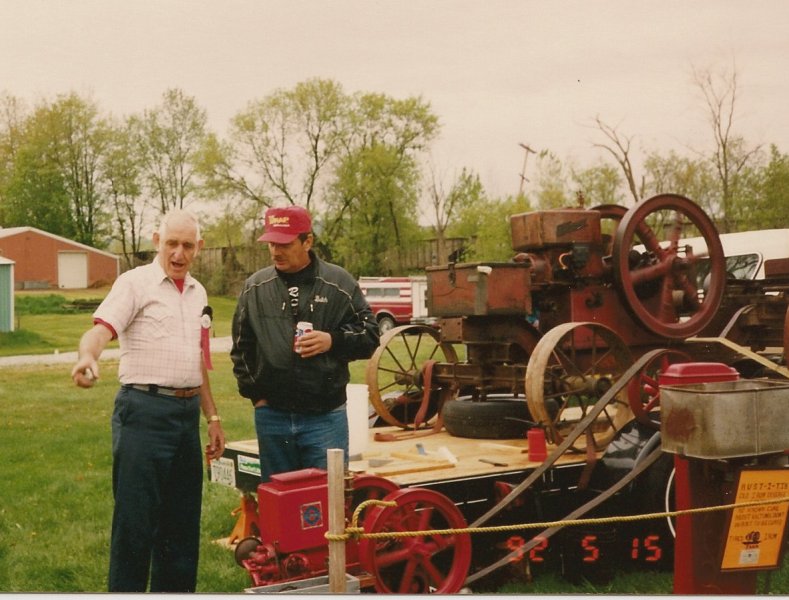 man pointing out to onlooker part of antique engine