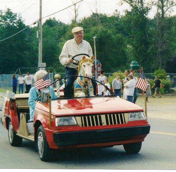 man driving a car modified with a carousel horse as steering wheel