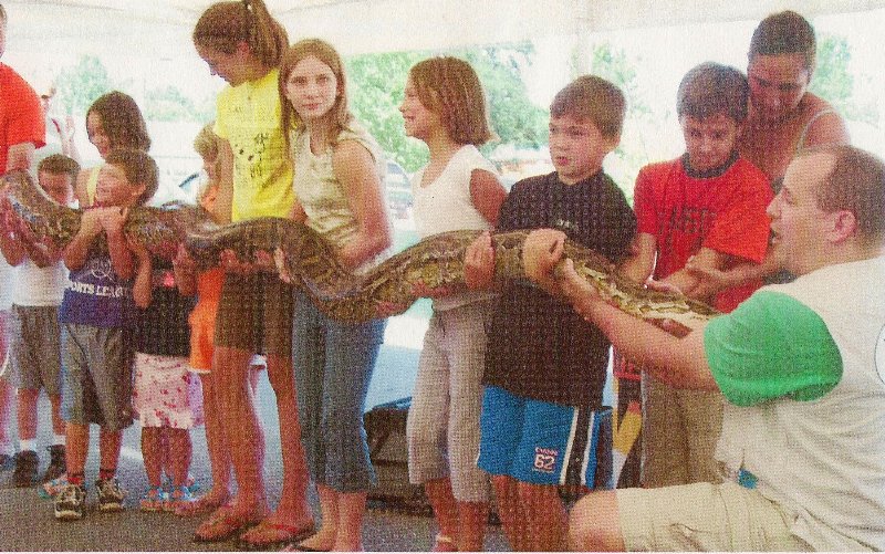 many children lined up holding a long snake
