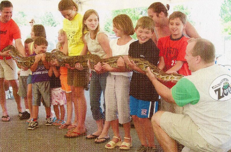 many children lined up holding a long snake