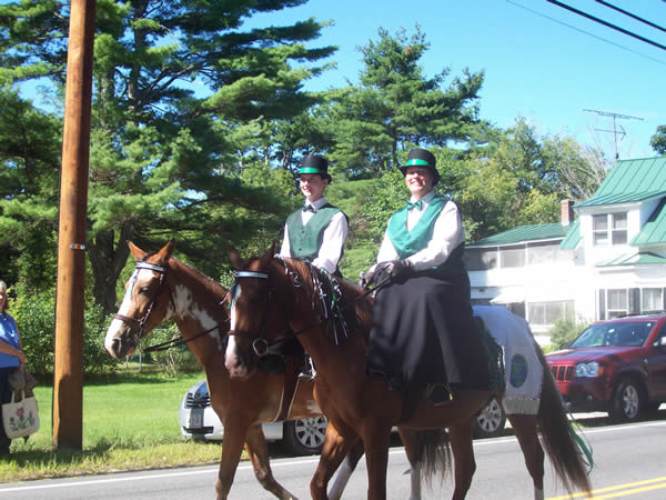 men dressed in fancy green vests and top hats on horses
